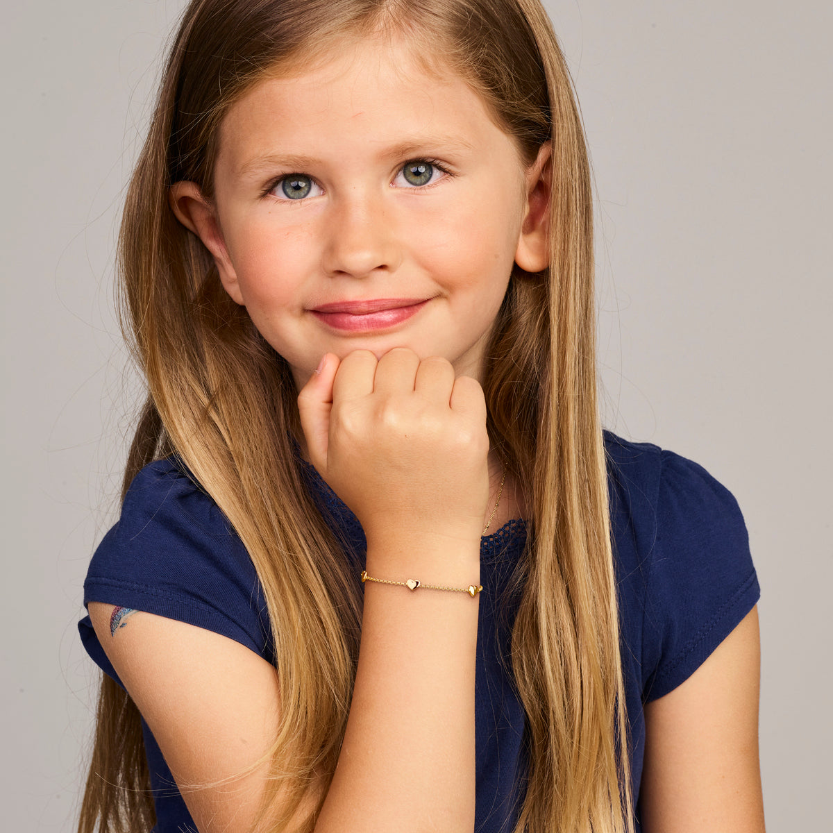 Model draagt de gouden kinderarmband met hartjes van 14 karaat om de pols.
