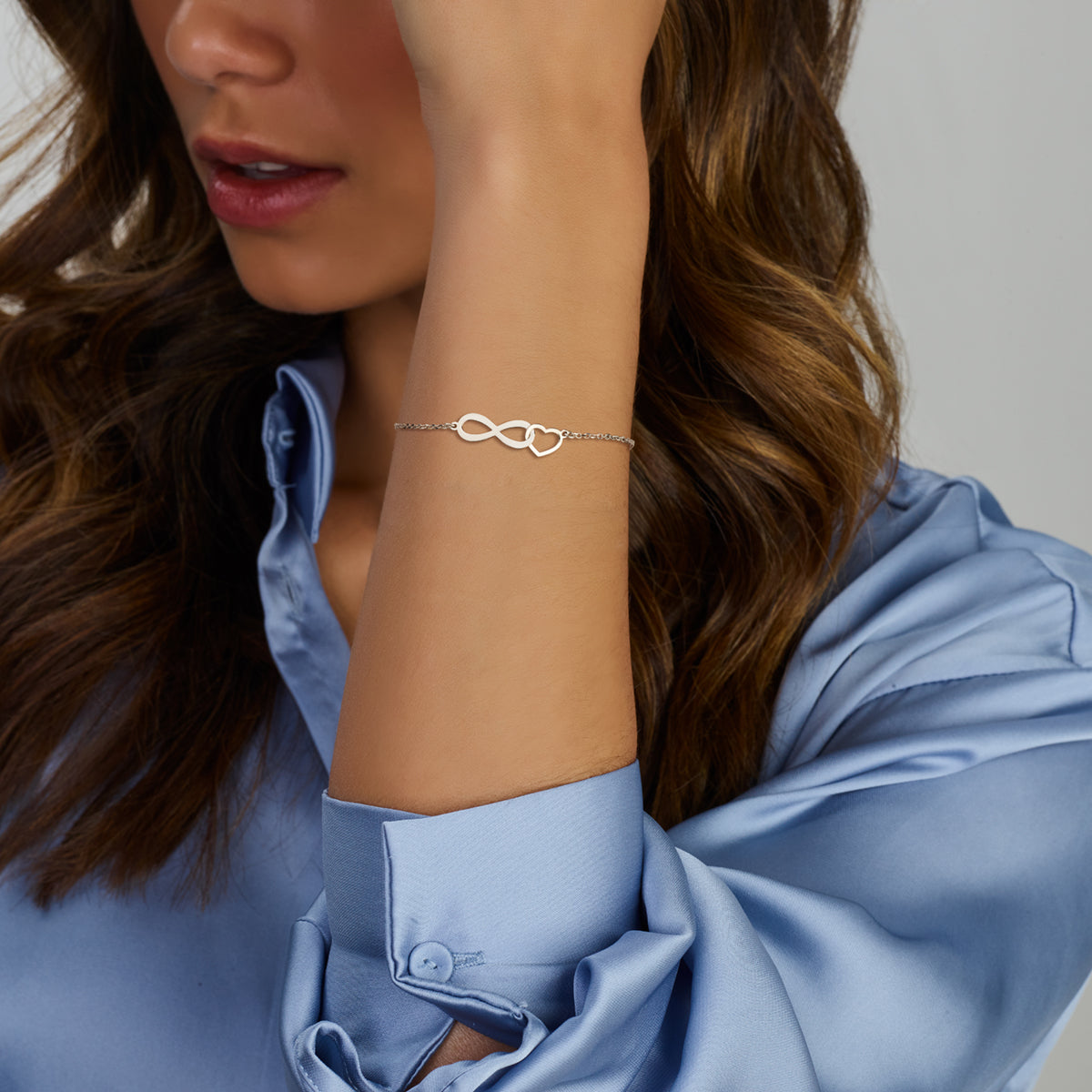 Model draagt de zilveren infinity armband met hartje om de pols.
