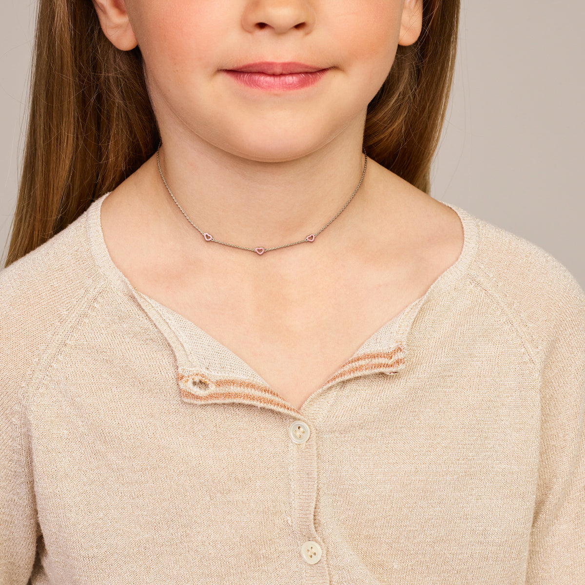 Model draagt de zilveren kinderketting met roze hartjes om de hals.