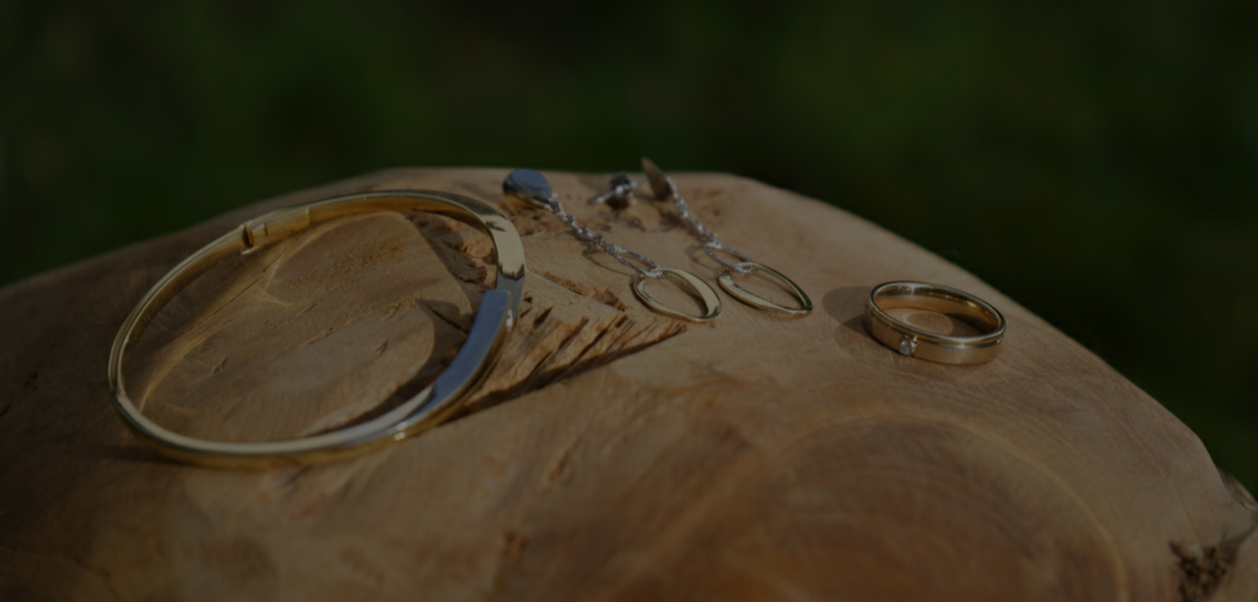 Een gouden armband, oorhangers en een ring te zien op een houten structuur.