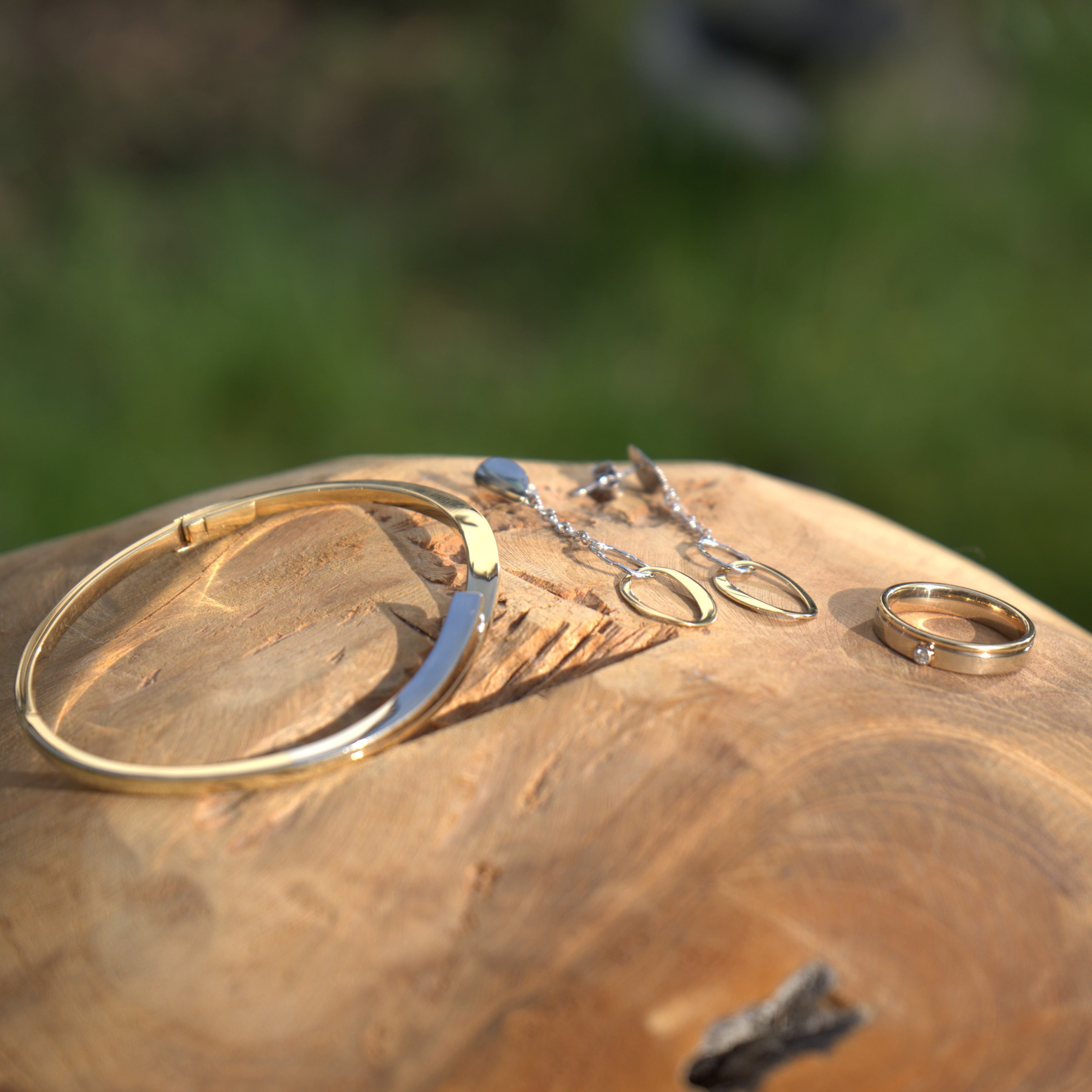 Een 14 karaat geelgouden armband, oorbellen en ring met diamant weergegeven in een natuurlijke setting. Ontdek alle gouden sieraden bij Clary