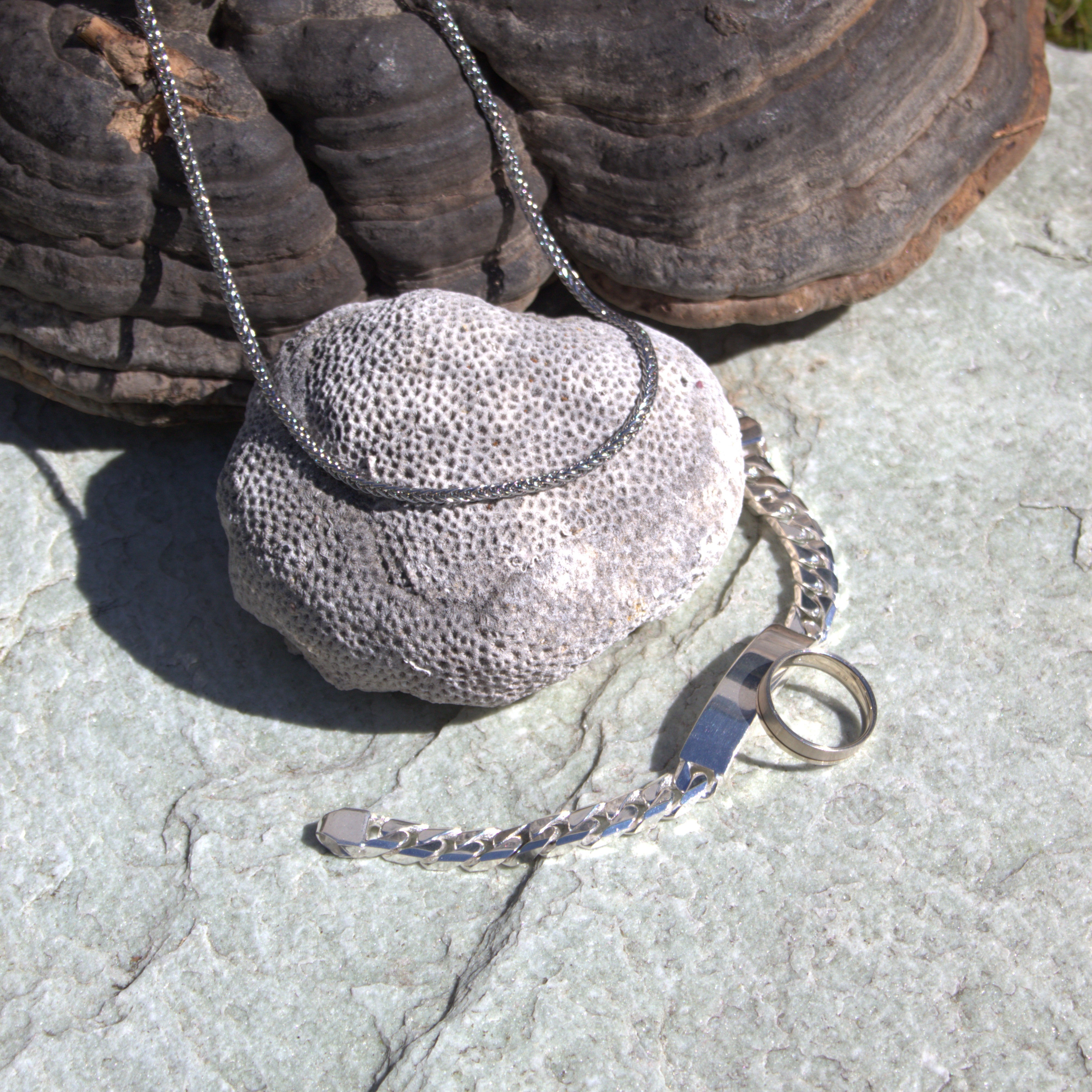 Verschillende heren sieraden weergegeven in een mooie natuurlijke setting. Er is een witgouden herenring, een zilveren schakelarmband voor heren en een halsketting te zien. Ontdek alle heren sieraden bij Clary.