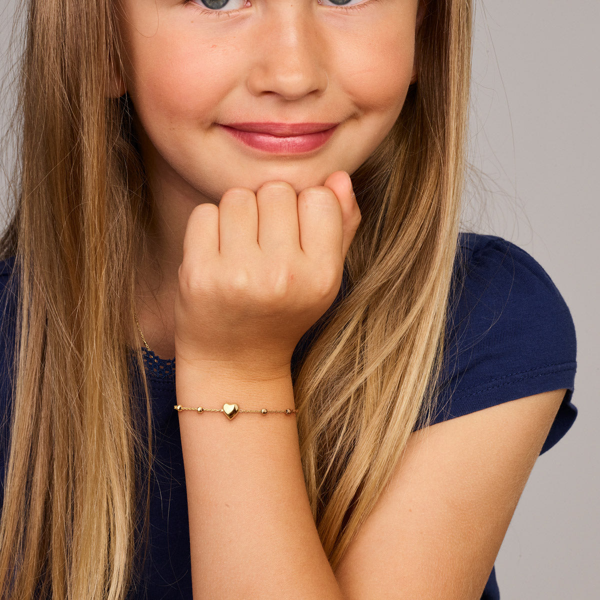 Model draagt de gouden kinderarmband met hartje en bolletjes van 14 karaat om de pols.