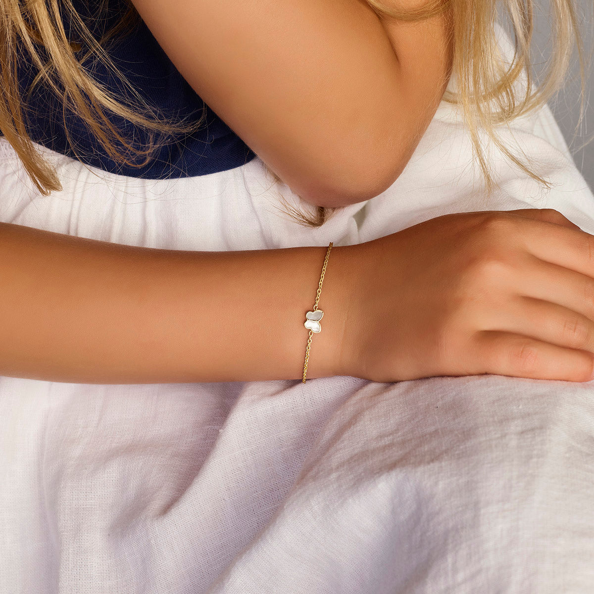 Model draagt de gouden kinderarmband met vlinder en parelmoer om de pols.