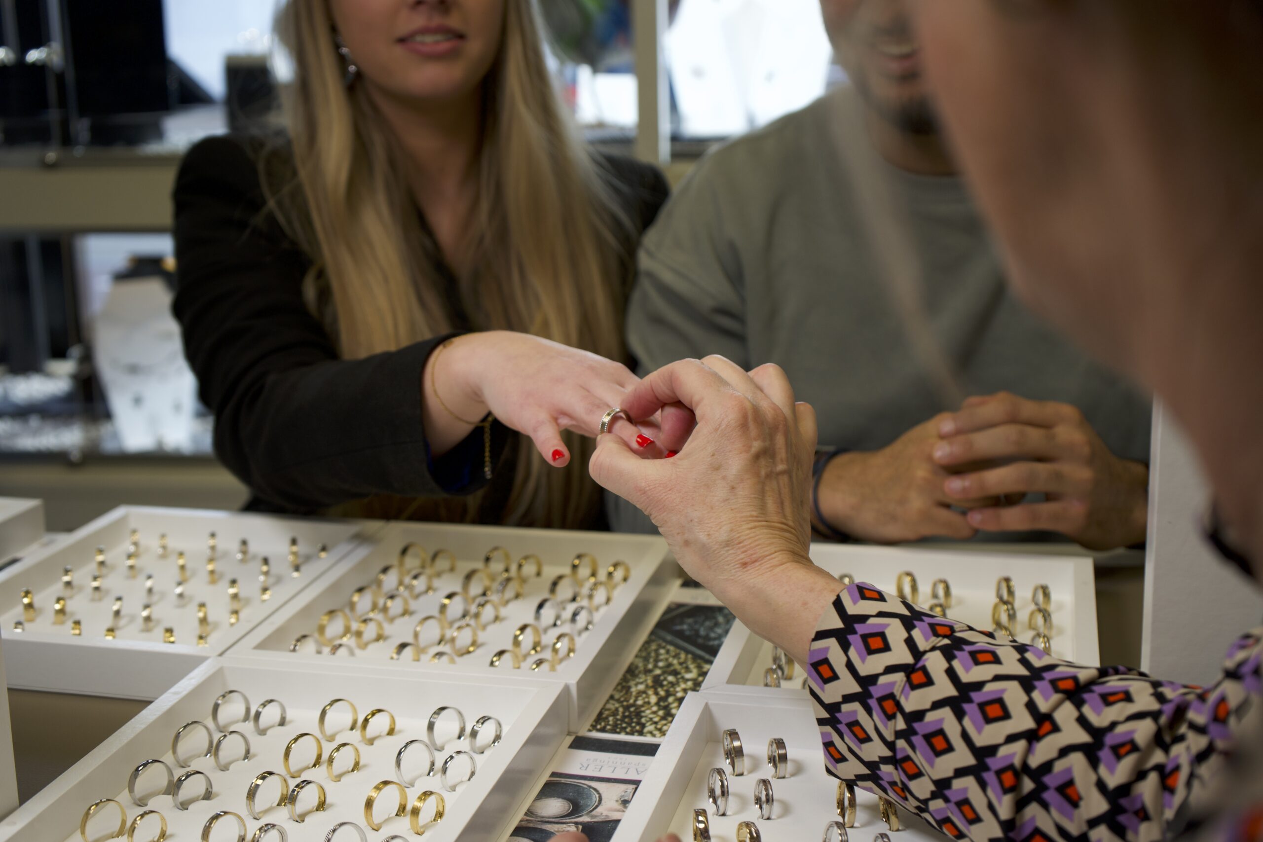 Een goudsmid geeft een koppel advies over gouden trouwringen in een warm en ambachtelijk atelier.
