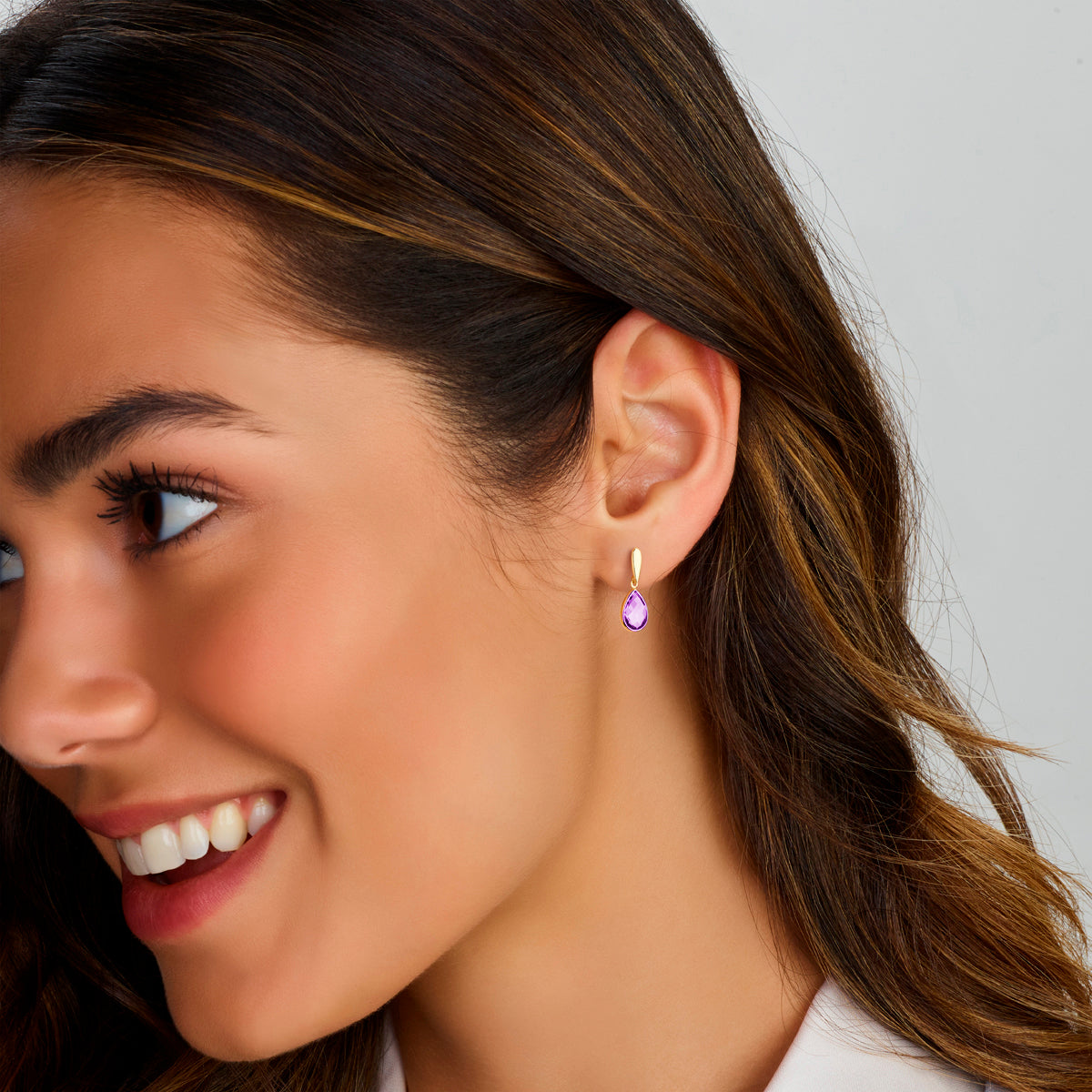 Een model draagt de gouden 'Gioia' oorbellen met paarse steentjes die prachtig glanzen.
