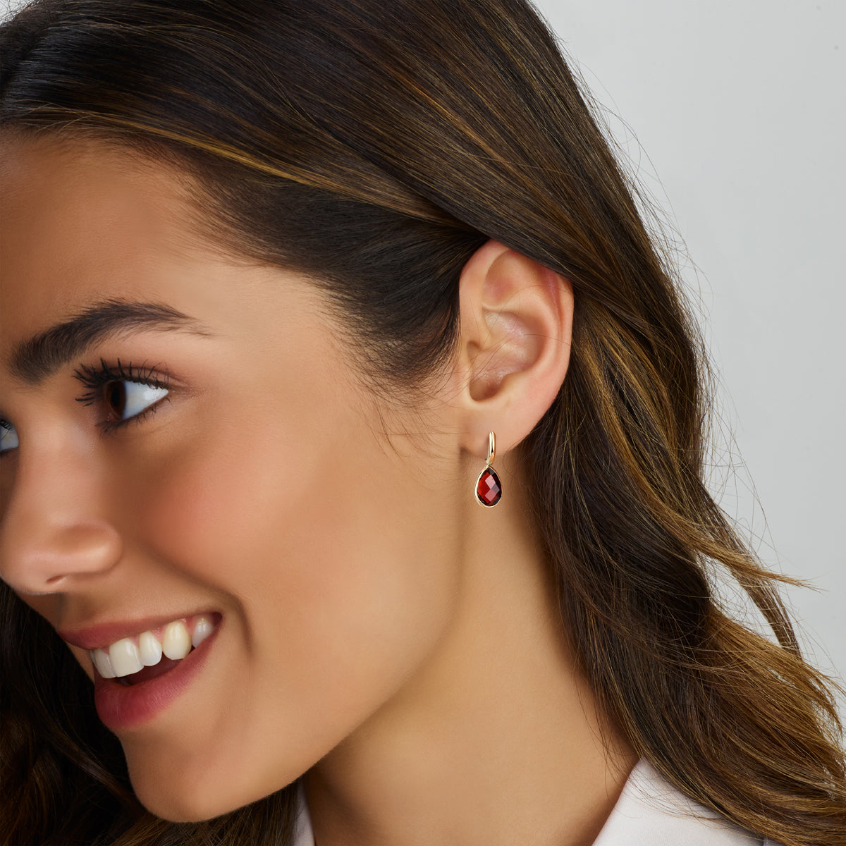 Een model draagt de 14k gouden 'Gioia' oorhangers, waarbij de rode edelstenen elegant en glanzend langs het gezicht vallen.