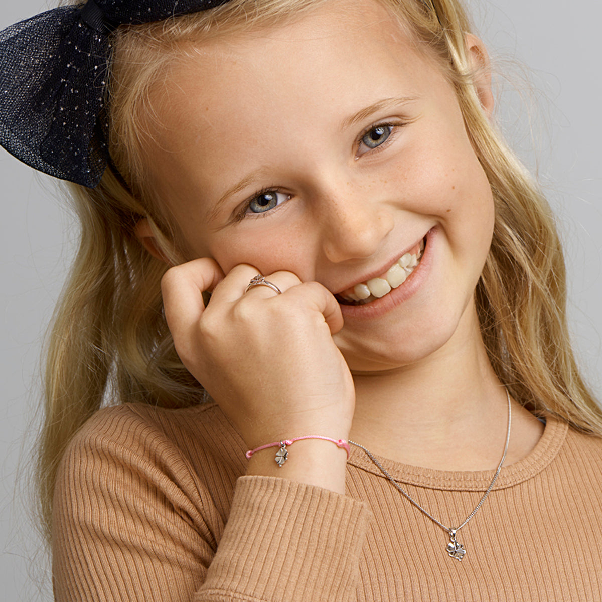 Een vrolijk kind model draagt de zilveren 'Feli' gelukshanger om de grootte te tonen.